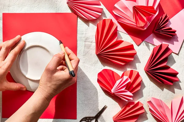Woman hands making paper hearts. Origami garland. Symbol of love for valentines day, happy birthday, greetings, Mothers day, Women\'s day. Diy. Step by step. Step one.
