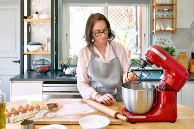 Mutfakta önlük giyen, kurabiye pişiren bir kadın. Ev hanımı bir kase gezegen mikserine yumurta kırıyor. Ev yapımı hamur işleri veya pasta..