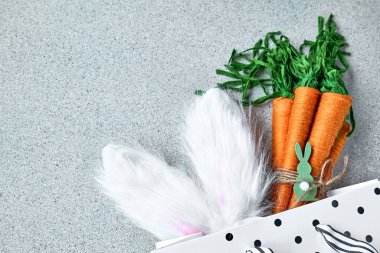 Tavşan kulakları ve yün iplik havuçları açık mavi arka planda beyaz kağıt torbada. Paskalya için minimalist dekor. El yapımı el işi projesi. Bayram ve Paskalya alışverişi kavramı.