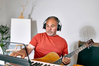 Akustik gitar çalıp evde şarkı söyleyen, kulaklık takan dalgın, olgun bir adam. Müzik hobisi. Yaratıcı bir eğlence. Kendini ifade etme kavramı.