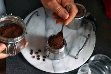 Adam mutfaktaki kahveye klasik İtalyan kahvesi hazırlıyor, moka demliğinin hunisini öğütülmüş kahveyle dolduruyor. Kahve freni. Sabah alışkanlığı.