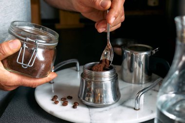 Adam mutfaktaki kahveye klasik İtalyan kahvesi hazırlıyor, moka demliğinin hunisini öğütülmüş kahveyle dolduruyor. Kahve freni. Sabah alışkanlığı.