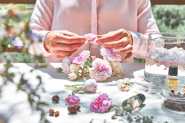Cam kasede pembe gül yapraklarıyla gül suyu hazırlayan kadın. Cilt bakımı, kaplıca, doğal güzellik tedavisi, ev yapımı kozmetik ürünleri. Seçici odak.