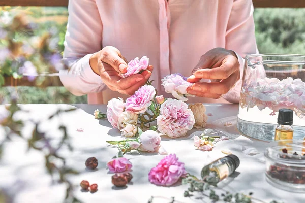 Cam kasede pembe gül yapraklarıyla gül suyu hazırlayan kadın. Cilt bakımı, kaplıca, doğal güzellik tedavisi, ev yapımı kozmetik ürünleri. Seçici odak.
