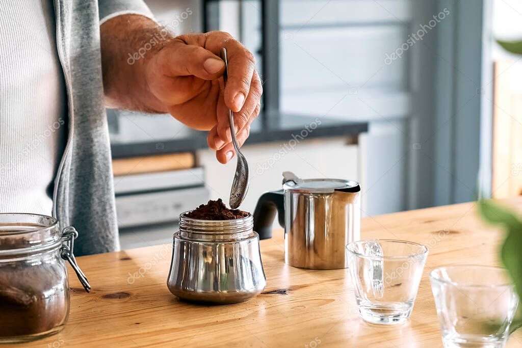 Man preparing classic Italian coffee in the mocha in the kitchen, filling funnel of a moka pot with ground coffee. Coffee brake. Morning habit.