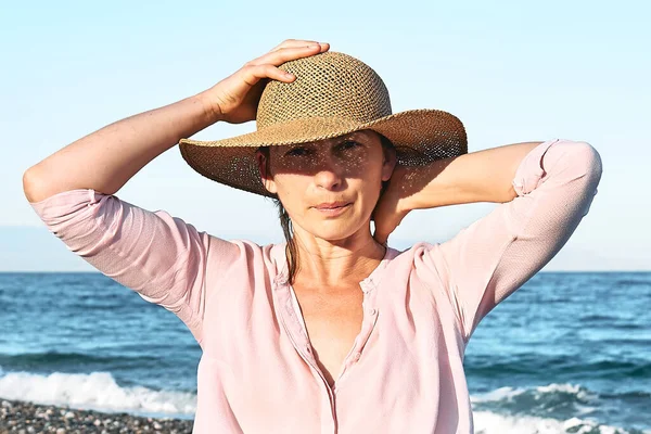 Portrait of happy middle aged woman wearing straw hat enjoying on sea. Wellness, success, freedom and travel concept. Trip in summertime.