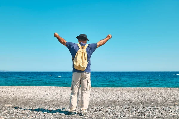 Happy tourist man enjoying freedom with open hands on sea. Wellness, success, freedom and travel concept. Trip in summertime.