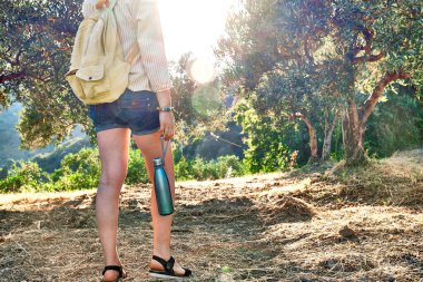 Olive Grove 'da elinde çelik termal şişeyle gezen, sırt çantasıyla gezen ya da dışarıda egzersiz yapan bir kadın. Aktif insanlar, yürüyüş, sağlıklı yaşam tarzı ve uyum kavramı. Doğayla birlik.