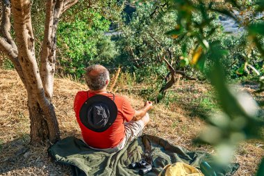 Turist zeytinlikte dinleniyor, dağ manzarası önünde meditasyon yapıyor ya da dışarıda egzersiz yapıyor. Aktif insanlar, seyahat, yürüyüş, sağlıklı yaşam tarzı ve uyum kavramı. Doğayla birlik.