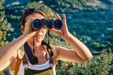 Zeytin koruluğunda dinlenen turist kadın dürbünden bakıyor.