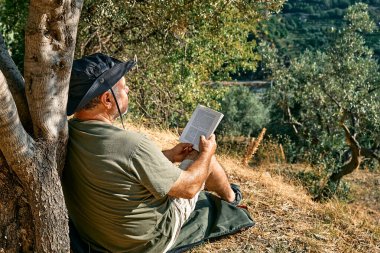 Sakallı turist, ağacın altında kitap okuduktan sonra dinleniyor, güneşli bir günde sonbahar parkında roman okuyor. Aktif insanlar, sağlıklı yaşam tarzı ve uyum kavramı. Refah ve doğa ile birlik.
