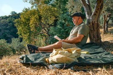 Sakallı turist, ağacın altında kitap okuduktan sonra dinleniyor, güneşli bir günde sonbahar parkında roman okuyor. Aktif insanlar, sağlıklı yaşam tarzı ve uyum kavramı. Refah ve doğa ile birlik.