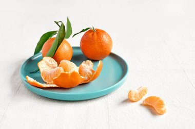 Fresh ripe juicy tangerines with leaves in blue plate on linen tablecloth. Citrus fruits for healthy eating and natural vitamins.