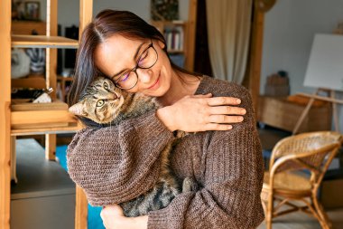 Middle-aged woman hugging cute tabby cat in indoor scene. Human-animal relationships. Funny home pet. Homeless pets.