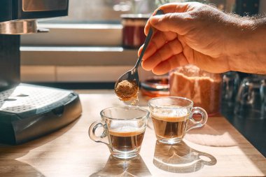 Kahverengi şekeri aromatik sıcak içecek espresso ile bardaklara koyan bir adam. Evdeki mutfakta espresso kahve makinesinde hazırlandı. Uyanış içkisi. Sabah alışkanlığı.