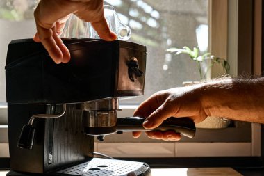 Hands of man making espresso in espresso coffee machine in the kitchen at home. Awakening hot drink. Morning habit.