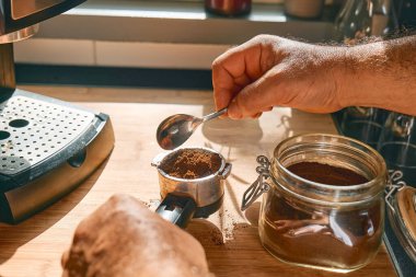Hands of man making espresso in the kitchen, filling funnel of espresso coffee machine pot with ground coffee. Morning habit.