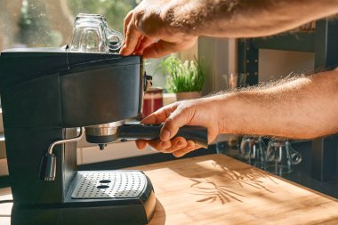 Hands of man making espresso in espresso coffee machine in the kitchen at home. Awakening hot drink. Morning habit.