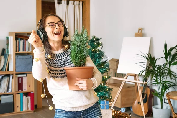 Young woman listen christmas music with headphones and dancing in living room while decorated it with christmas decoration. Funny winter holidays.