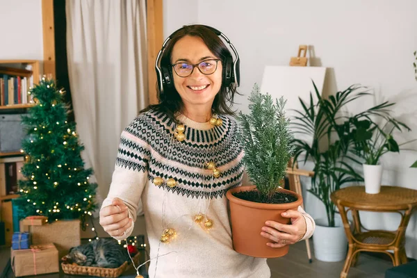 Young woman listen christmas music with headphones and dancing in living room while decorated it with christmas decoration. Funny winter holidays.