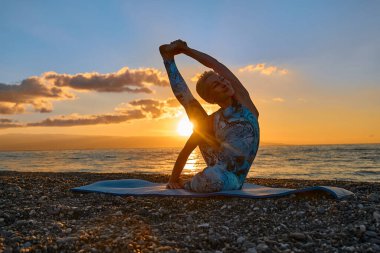 Gün doğumunda sahilde yoga yapan genç bir kadın. Uyum, refah, meditasyon, sağlıklı yaşam tarzı, rahatlama, yoga, kişisel bakım, düşünceli meditasyon konsepti..