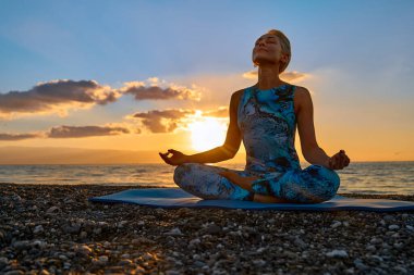 Gün doğumunda sahilde yoga yapan genç bir kadın. Uyum, refah, meditasyon, sağlıklı yaşam tarzı, rahatlama, yoga, kişisel bakım, düşünceli meditasyon konsepti..