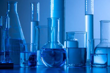 Mavi ışık altında deney tüpleri, şişe, silindirler ve test tüpleri gibi laboratuvar ekipmanları