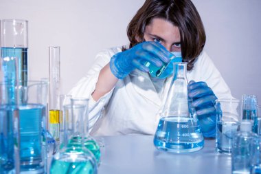 Genç bilim adamı bir laboratuarda şişelerle ve şişelerle sıvıları karıştırıyor.