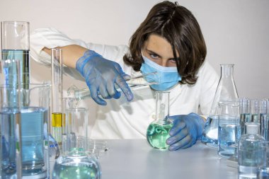 Genç bilim adamı bir laboratuarda şişelerle ve şişelerle sıvıları karıştırıyor.