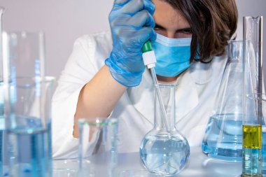 Genç bilim adamı bir laboratuarda pipetle örnek alıyor.