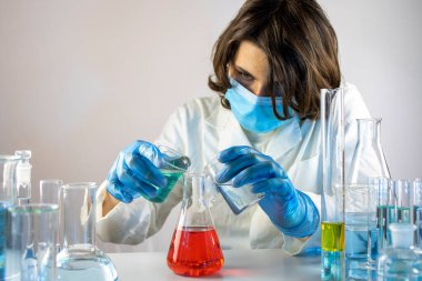 Genç bilim adamı bir laboratuarda şişelerle ve şişelerle sıvıları karıştırıyor.