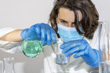 Genç bilim adamı bir laboratuarda şişelerle ve şişelerle sıvıları karıştırıyor.