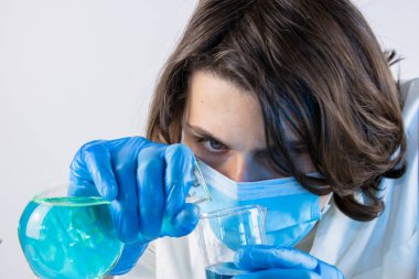 Genç bilim adamı bir laboratuarda şişelerle ve şişelerle sıvıları karıştırıyor.