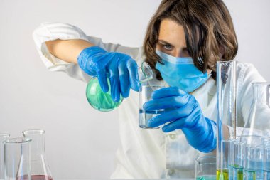 Genç bilim adamı bir laboratuarda şişelerle ve şişelerle sıvıları karıştırıyor.