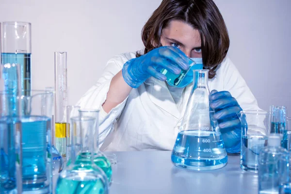 Genç bilim adamı bir laboratuarda şişelerle ve şişelerle sıvıları karıştırıyor.