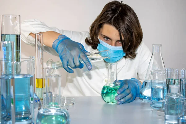 Genç bilim adamı bir laboratuarda şişelerle ve şişelerle sıvıları karıştırıyor.