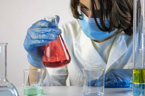 Genç bilim adamı bir laboratuarda şişelerle ve şişelerle sıvıları karıştırıyor.