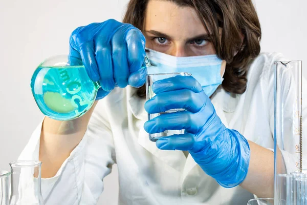 Genç bilim adamı bir laboratuarda şişelerle ve şişelerle sıvıları karıştırıyor.