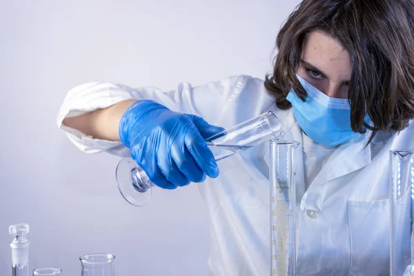 Genç bilim adamı bir laboratuarda şişelerle ve şişelerle sıvıları karıştırıyor.