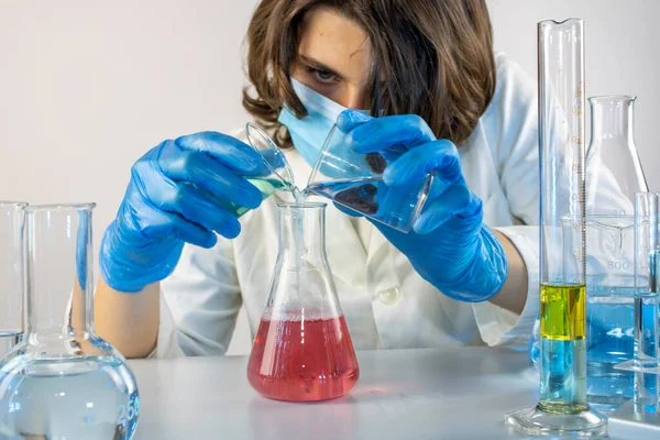 Genç bilim adamı bir laboratuarda şişelerle ve şişelerle sıvıları karıştırıyor.