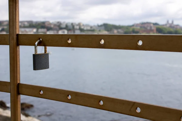 Metal padlock placed on a railing by the sea