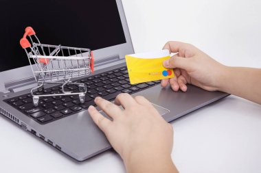 Bilgisayar ve küçük oyuncak alışveriş arabası masada. İnternet alışverişi konsepti. Kadın internet alışverişi yapıyor..