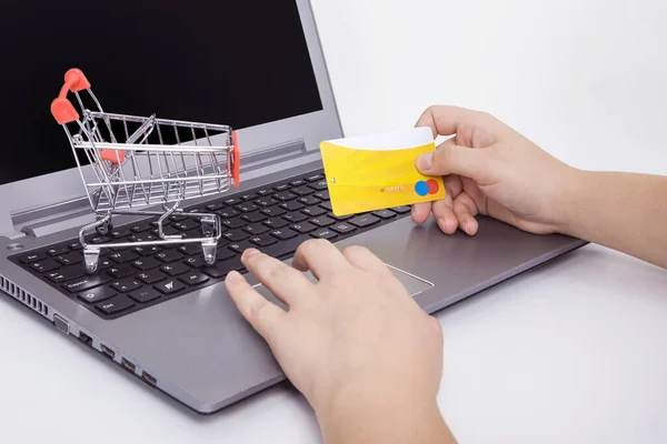 Bilgisayar ve küçük oyuncak alışveriş arabası masada. İnternet alışverişi konsepti. Kadın internet alışverişi yapıyor..