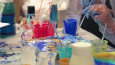 Bir kadın plastik bir içecek tüpüne üfleyerek sanat yapıyor ve onu fırçayla süpürüyor..