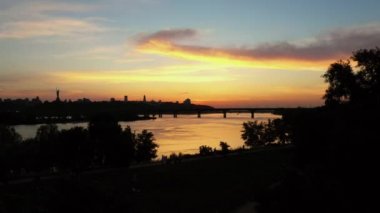 Nehir, köprü ve alacakaranlık günbatımı gökyüzü olan şehir parkı.