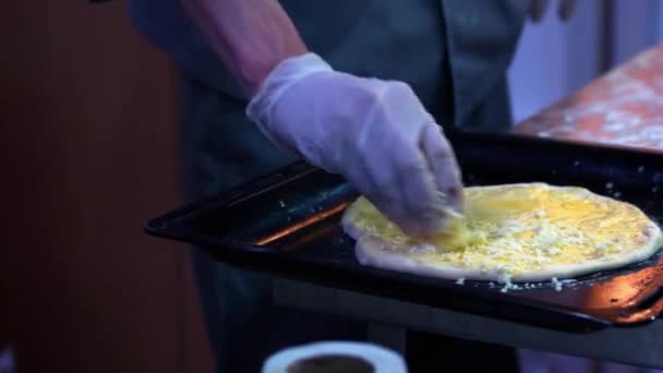 Κοντινό πλάνο μαγειρεύει τα χέρια προσθέτοντας τεμαχισμένο τυρί σε μια ζύμη πίτσα. — Αρχείο Βίντεο