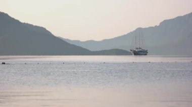 Deniz koyunda arka planda dağlar ve yatlar var..