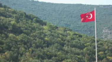 Rüzgarda dalgalanan Türkiye bayrağı. Arka planda güzel yeşil dağlar.