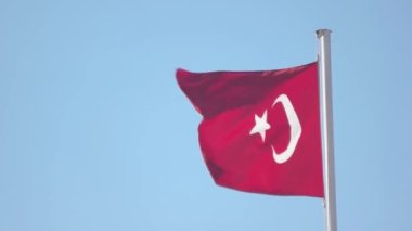 Rüzgarda dalgalanan Türkiye bayrağı. Arkaplanda açık mavi gökyüzü.