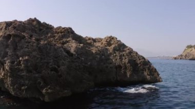 Denizde büyük bir kaya. Sakin deniz, mavi gökyüzü ve arka planda dağlar..